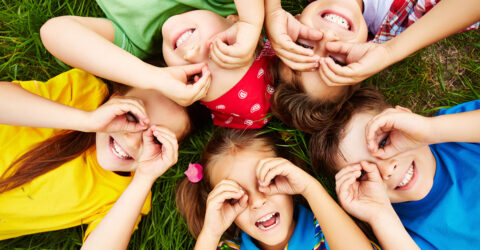 Cinq enfants sont allongés en cercles, leurs têtes se touchant, et ils font des grimaces.